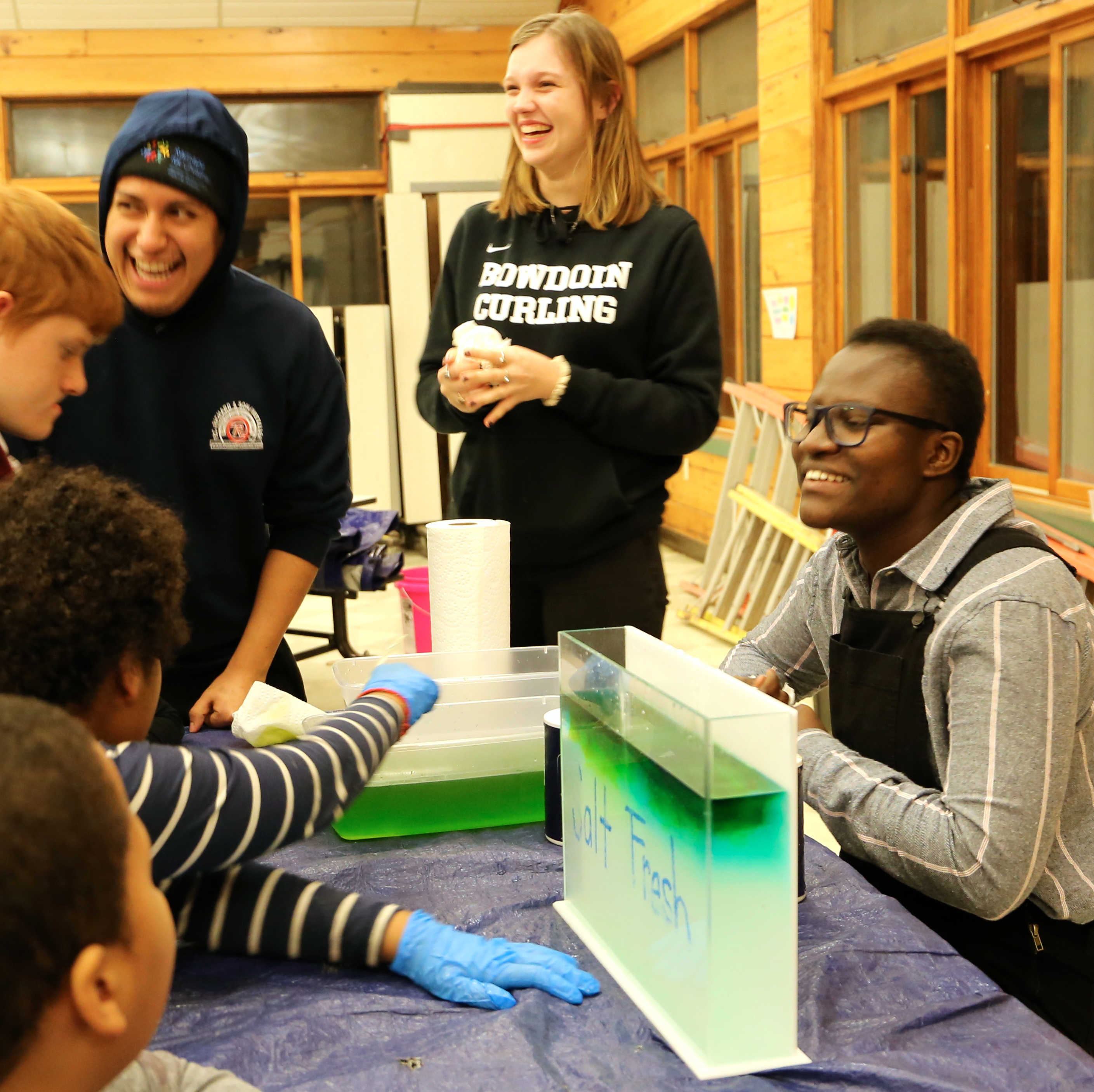 STEM Night Out students standing around a table with test tubes, laughing.; Volunteer with Us: STEM Night Out