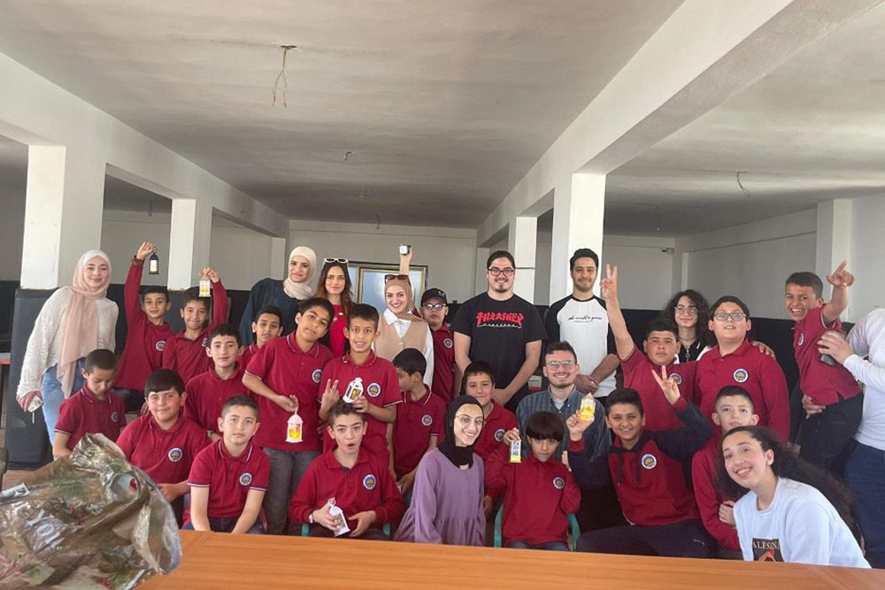 Group of elementary students with college student volunteers in a large room inside a building smiling and posing for camera.; Al-Quds Bard College Civic Engagement Program Awarded First Place in the 2024&nbsp;MacJannet&nbsp;Prize for Global Citizenship