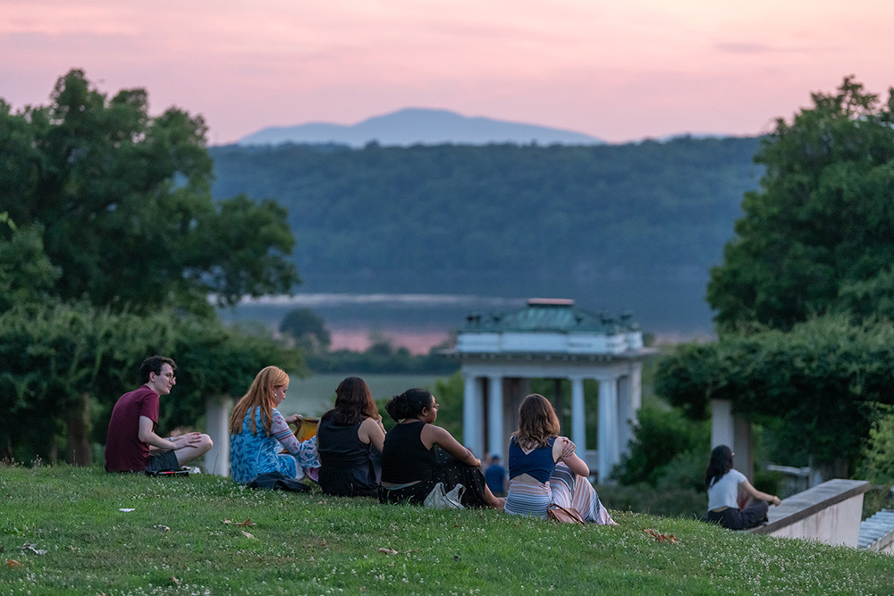 Students sitting on lawn in historic gardens at sunset by the Hudson River.