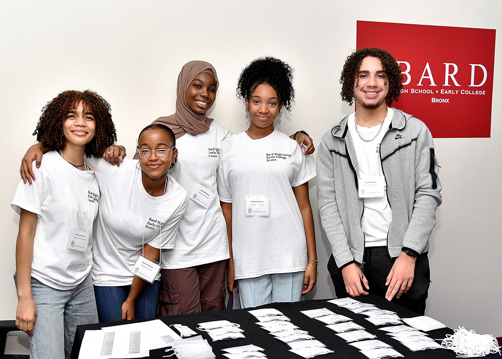 Five high school students standing behind a table, smiling and facing camera.