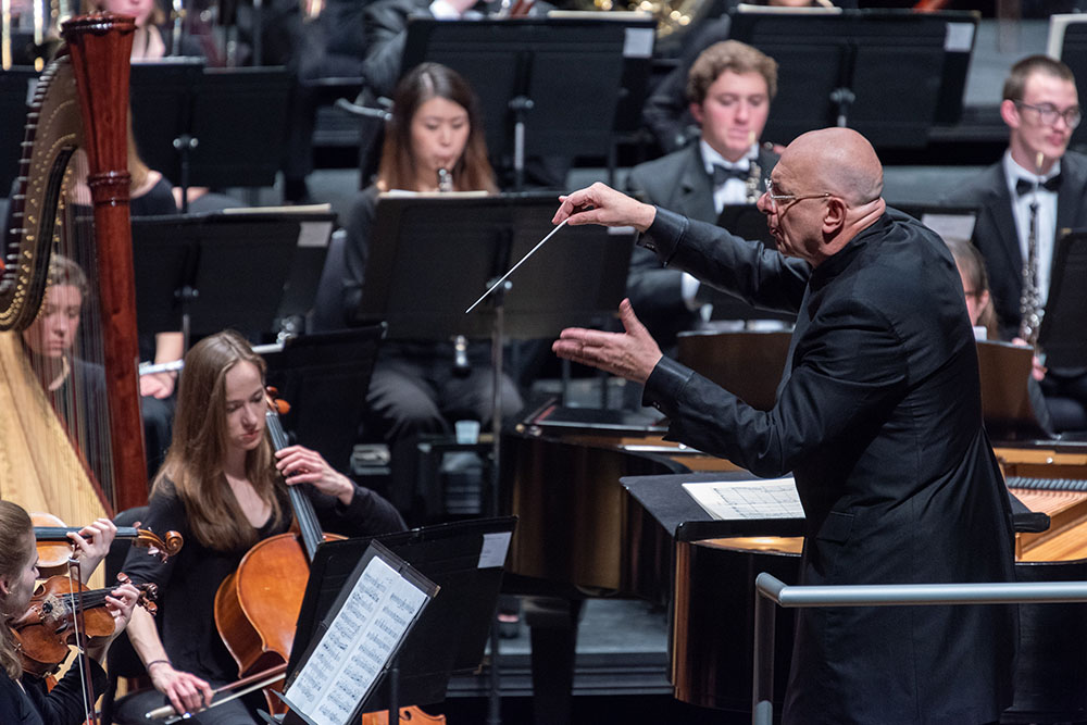 Close up on conductor leading the strings section of a classical orchestra.