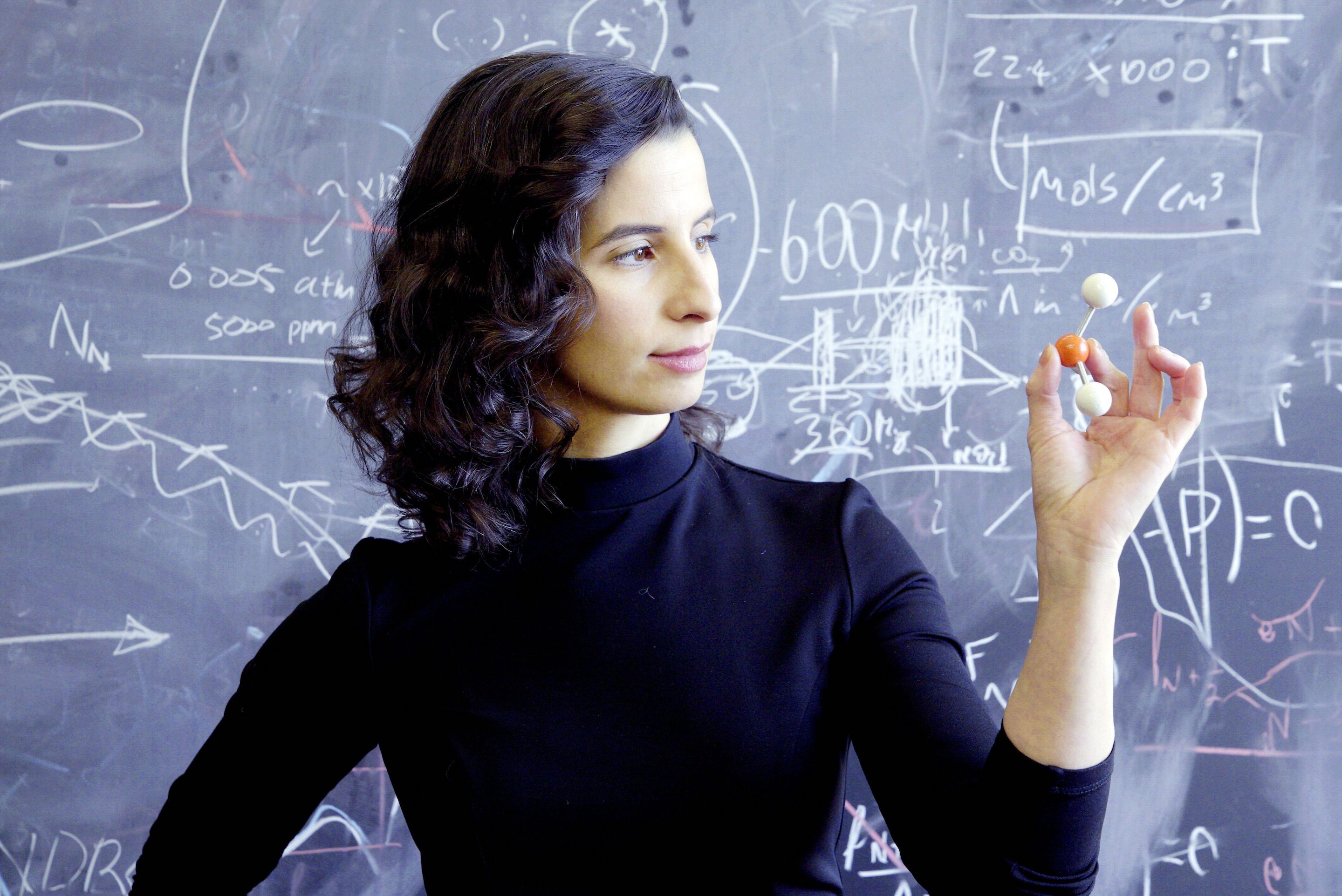 A woman gives a demonstration in front of a black board during a lesson in physics.