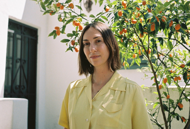 A woman in yellow stands beneath a citrus tree