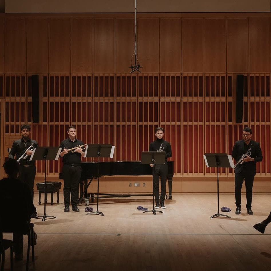 Four musicians standing on stage, holding instruments.; Trumpet Studio Recital