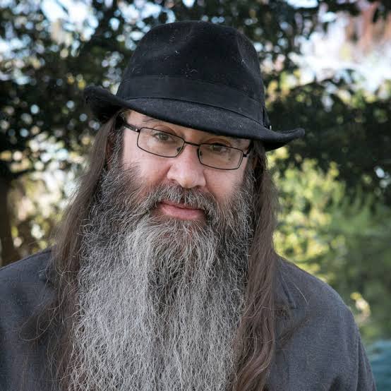 A headshot of a man in a hat and glasses standing in front of a tree.; Jews on Campus Pick a Side: On the Demand That Jews Be Public