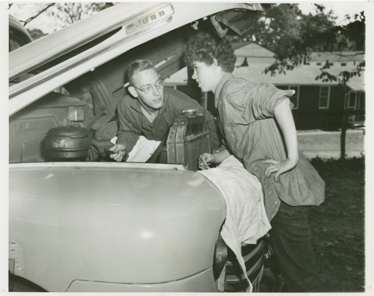 Two people work on the engine of an old Ford truck.