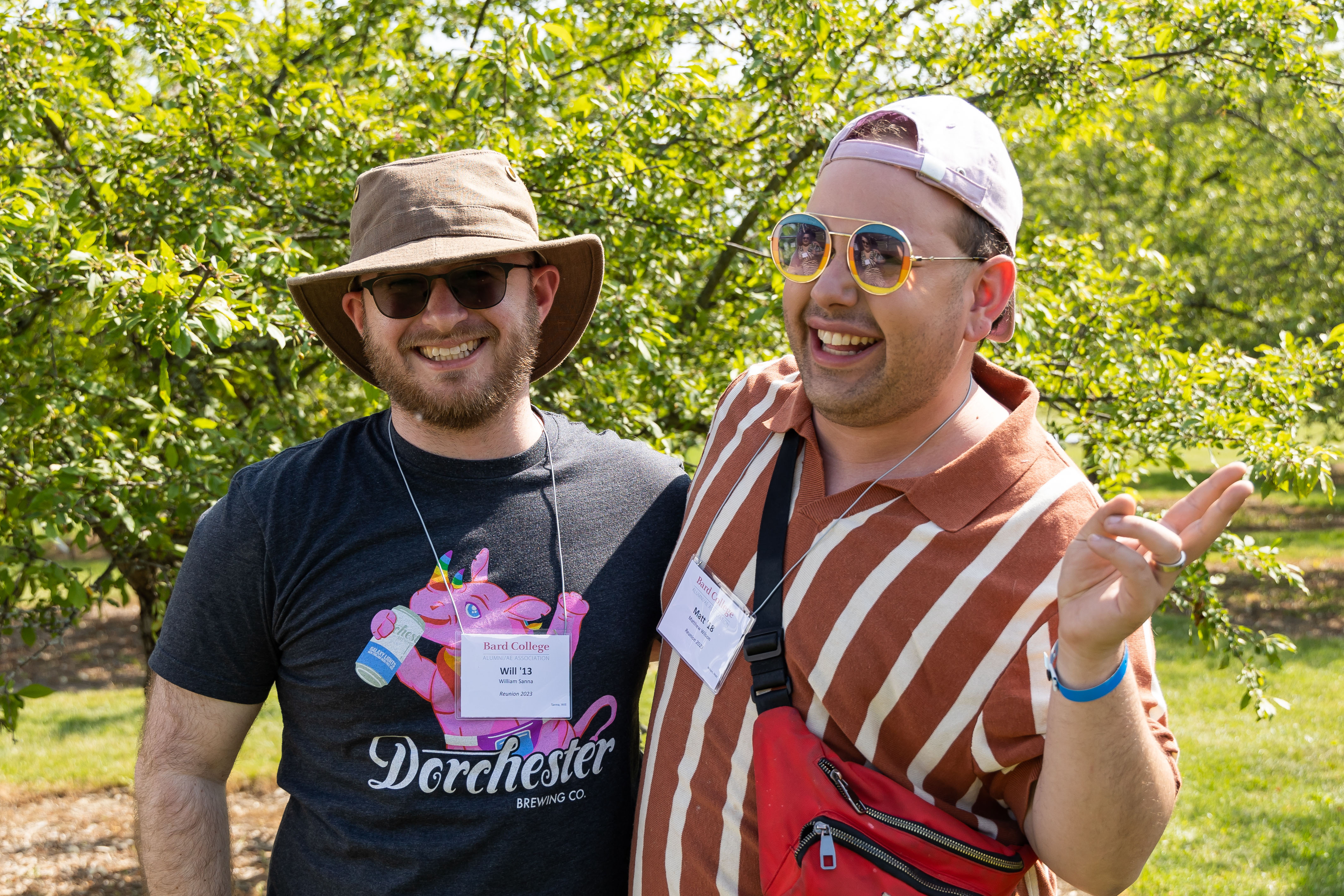 Two men smile and pose for the camera with greenery behind them.