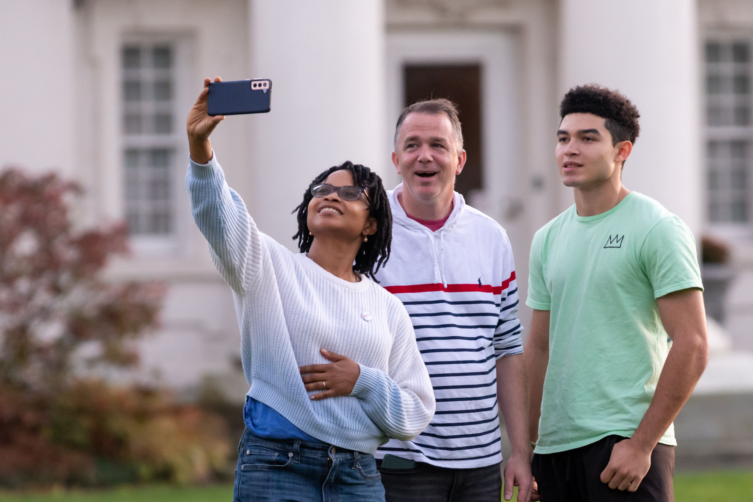 A family poses to take a selfie outside a white building.