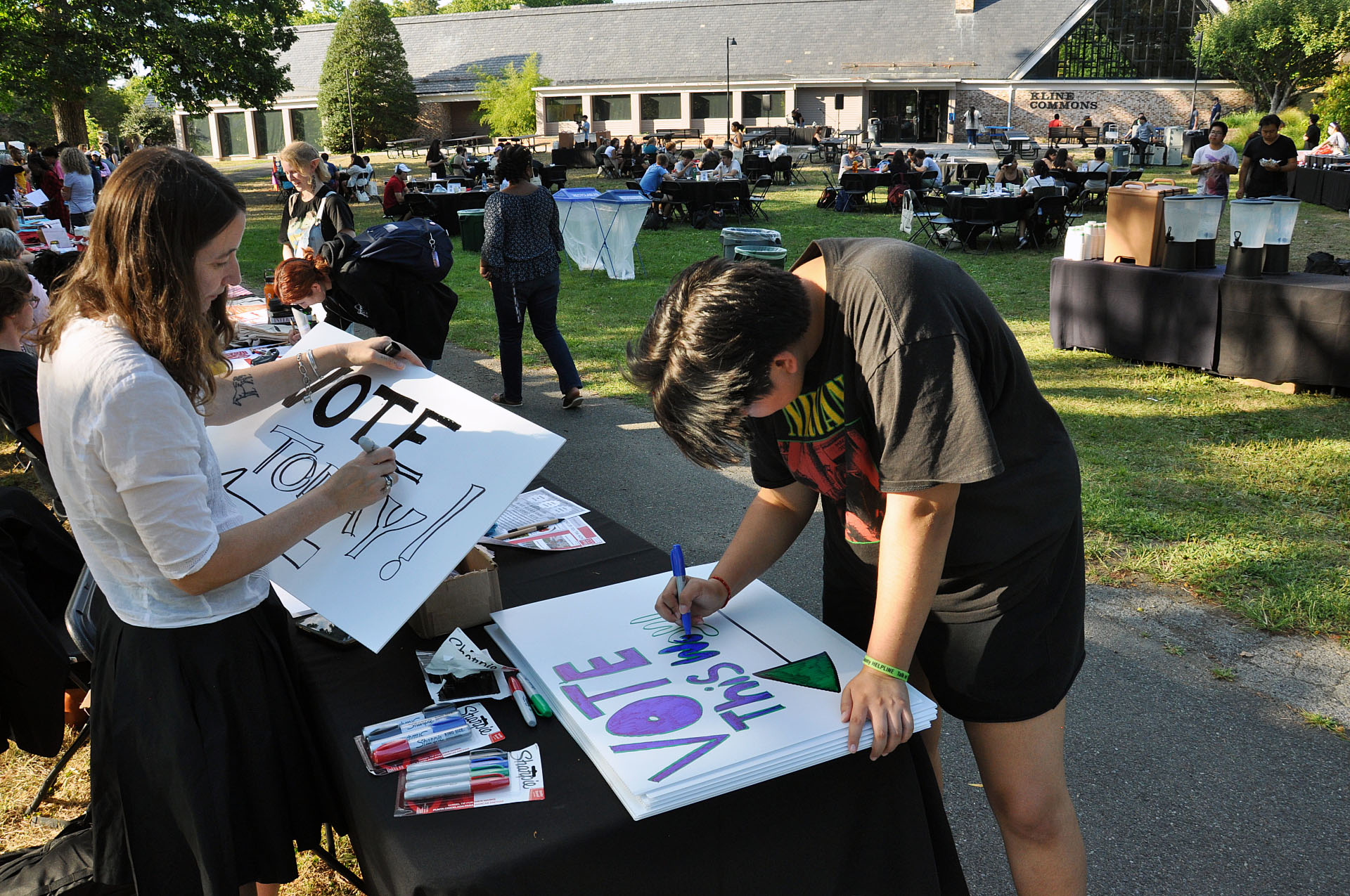 A student prepares a poster to encourage students to vote outside at a picnic table.